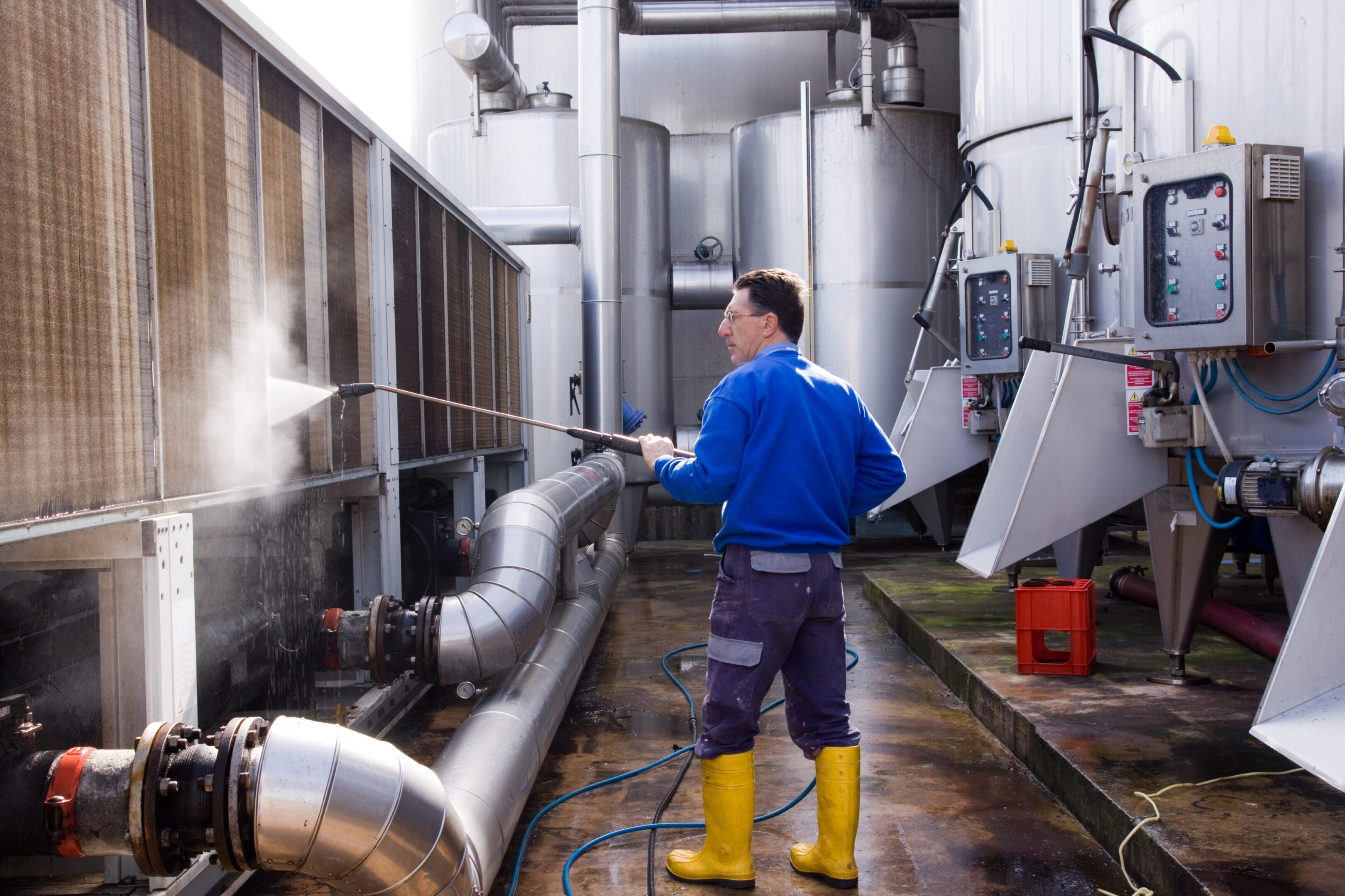 Worker cleaning industrial equipment with pressure washer.