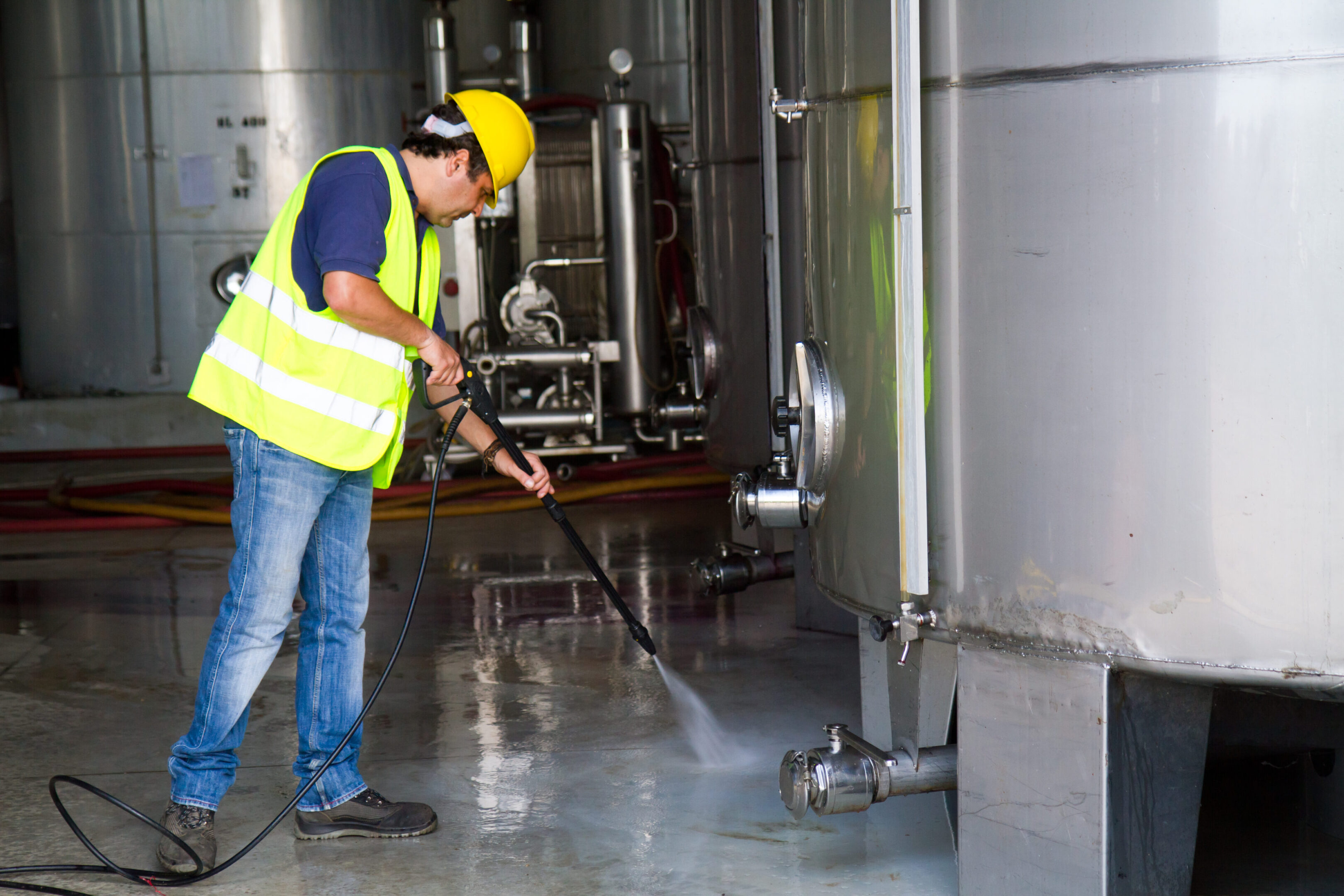 Worker pressure washing industrial equipment.