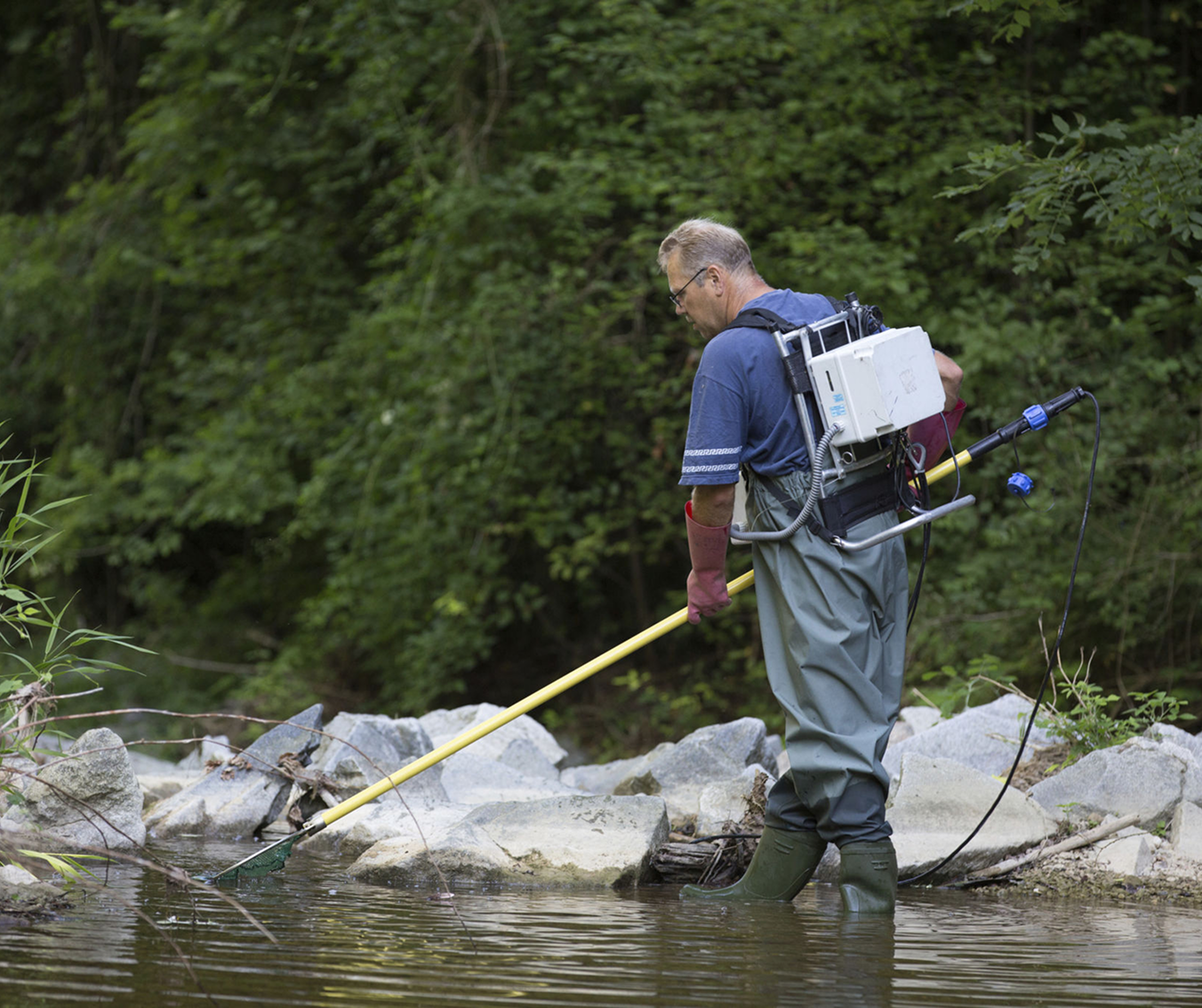 Scientist testing water near industrial tanks.